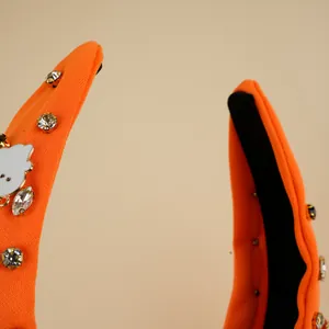 Detail eines orangefarbenen Strickstirnbands mit Kristallen und weißem Emaille-Anhänger