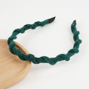 Détail d'un bandeau en tricot vert foncé avec fils scintillants et design tressé torsadé