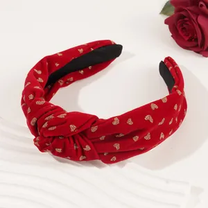 Close-up of red velvet knotted headband with gold glitter heart patterns and soft texture