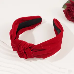 Red velvet knotted headband with gold glitter detail on a white textured base