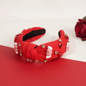 Detalle de diadema anudada roja con pedrería, gemas de corazón y adornos de letras
