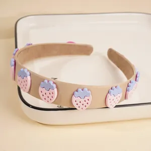 Detailaufnahme von khakifarbenem Stoffstirnband mit 3D-Erdbeeren auf weißem Porzellan