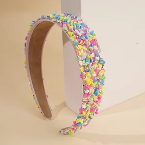 Detail eines bonbonfarbenen Stirnbands mit Herz-Pailletten und Perlen auf rosa Stoff