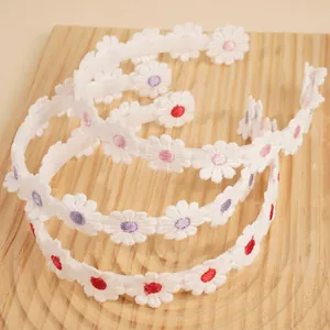 Detailed view of three white embroidered daisy headbands with colorful centers on wood