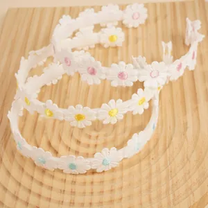 Detailed view of three embroidered daisy headbands in pink, yellow, and blue colors