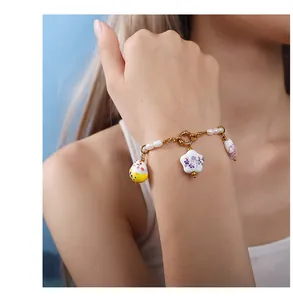 Close-up of ceramic lucky cat and floral charms on a pearl bracelet with gold chain