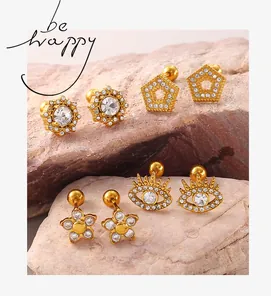 Détails de boucles d'oreilles dorées fleur et œil protecteur sur fond de pierres