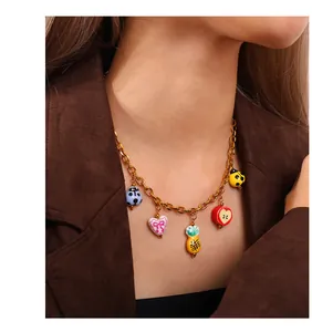 Close-up of golden necklace with colorful enamel ladybug and fruit charms on a model