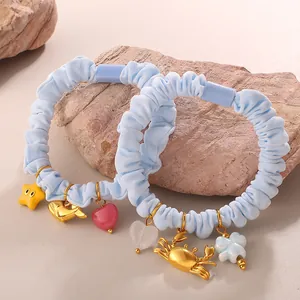 Blue ocean-themed scrunchie set with whale, crab, and star pendants on natural rock