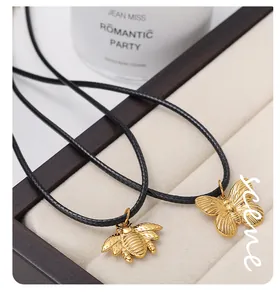 Detailed view of vintage gold bee and butterfly pendants on black cord in a velvet box