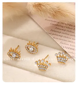 Détails de boucles d'oreilles œil et couronne dorées avec strass sur velours beige