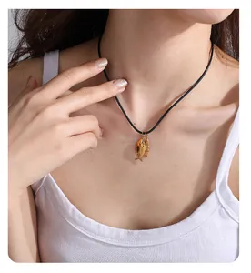 Detail von zwei Fischanhängern aus Goldmetall an einer schwarzen Kordelkette am Model