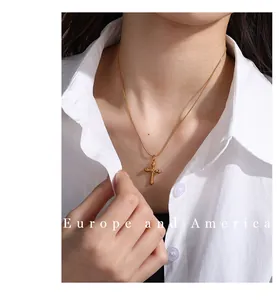 Close-up of golden cross pendant on a thin snake chain worn by a model in a white shirt