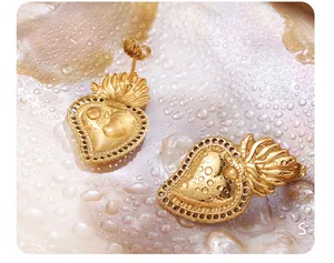 Macro view of gold sacred heart earrings with flame detail on a water-drop surface