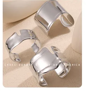 Dettaglio di ampi bracciali rigidi argento lucido con bordi ondulati e finitura a specchio