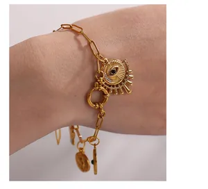 Dettaglio bracciale a catena in oro 18K con ciondolo occhio e monete vintage al polso