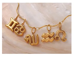 Detail view of five 18k gold zodiac pendants on a sleek snake chain over pearly background