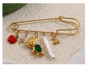 Vista macro de broche de imperdible dorado con colgantes de manzana, oso y perla fina