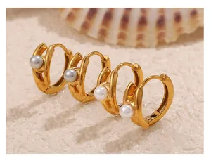 Detail of 18k gold plated hoop earrings with white and grey pearls on sandy background