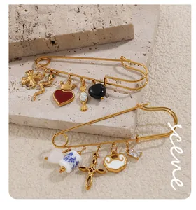 Detalle de broches de imperdible dorados con dijes de cruz, serpiente y corazón en piedra