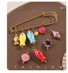 Detalle del broche dorado con colgantes coloridos de peces y corazones esmalte