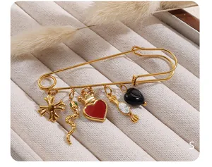 Detalle de un broche imperdible dorado con colgantes vintage de corazón, serpiente y cruz