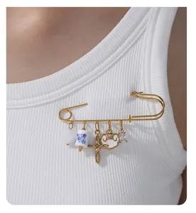Detalle de un broche de imperdible dorado con colgantes de corazón, nube y cristal brillante