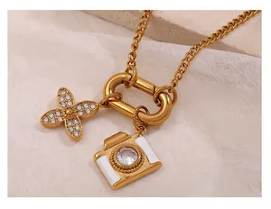 Dettaglio macro della collana dorata con chiusura a O, ciondolo fotocamera e fiore pavé