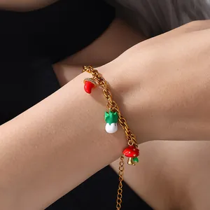 Gold chain bracelet with mushroom and vegetable enamel charms worn on a wrist