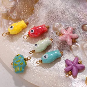 Colorful ceramic fish and starfish pendants with 18K gold loops on a pearl shell background