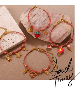 Detail of red woven bracelets with colorful gold enamel charms on a sandy stone background