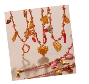 Close-up of woven rope jewelry with enamel strawberry, bee and cherry charms