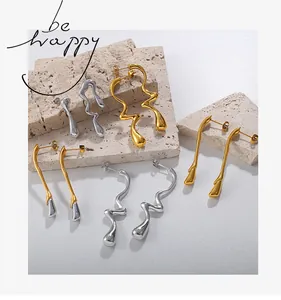 Détail de boucles d'oreilles irrégulières en or et argent sur pierre beige