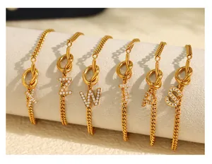 Detail van gouden knooparmbanden met zirkonia ingelegde letterhangers X Z W T P S