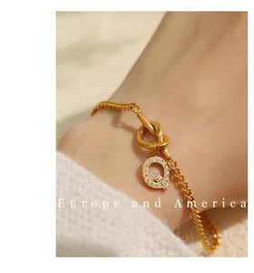 Detailweergave van goudkleurige schakelarmband met kristallen letter Q en knoopontwerp