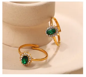 Dettaglio di due anelli regolabili dorati con zircone verde smeraldo e castone pavé