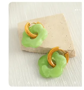 Macro detail of golden hoops with mint green resin flower pendants on stone