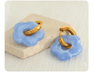 Macro detail of gold-plated hoop earrings with light blue marble texture flower pendants