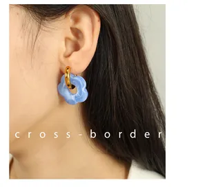Close-up of a blue camellia flower earring with golden hoop worn on a model's ear