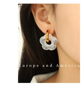 Close-up of gold hoop earring with white marble pattern flower pendant on ear