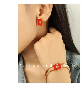 Nahaufnahme der roten Emaille-Ohrringe und des goldenen Schlangenkette-Armbands am Model