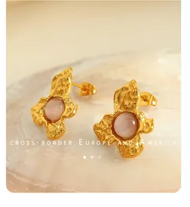 Detail of vintage irregular gold flower earrings with pink cat eye stone on a shell