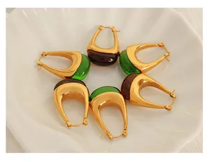 Detail view of U-shaped gold earrings with emerald green and amber resin charms