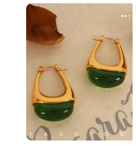 Detail of U-shaped gold earrings with dark green resin stones on a retro textured background