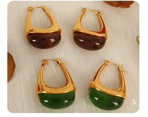 Macro shot of U-shaped gold earrings with amber brown and emerald green resin drops