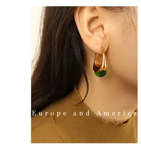Detail of a gold U-shaped earring with a green resin drop worn with a mustard sweater