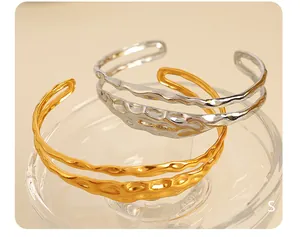 Macro view of textured 18K gold and silver plated hollowed-out cuff bangles on glass