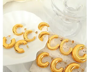 Macro view of polished 18K gold plated C-shape hoop earrings on a textured stone surface