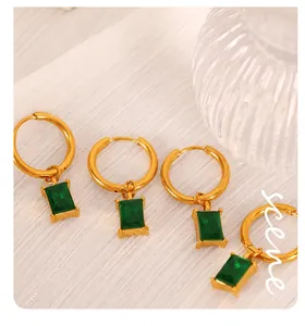 Detail of 18K gold-plated earrings with emerald-green rectangular stones on white fabric