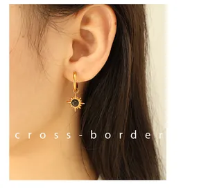 Detail of 18K gold hoop earrings featuring a sunburst pendant with black stone inlay